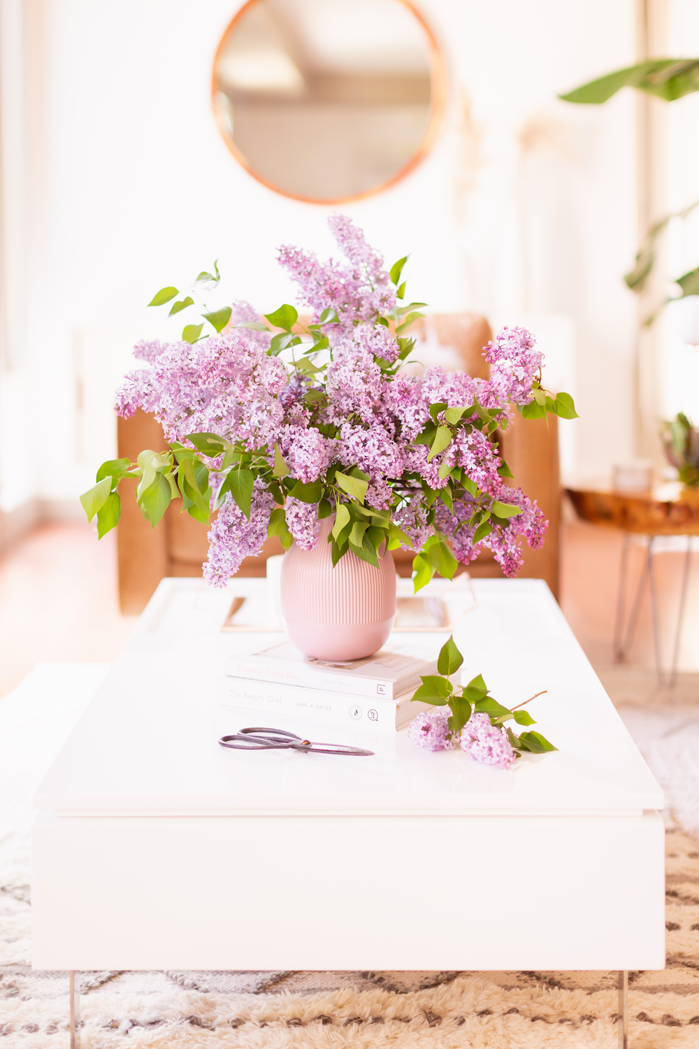 An oversized lilac bouquet and a pair of clippers on a white coffee table in JustineCelina’s light and airy mid century meets boho modern living room | DIY Lilac Flower Arrangement | How to Forage Lilacs | How to Prolong Lilac Vase Life | How to Arrange Lilacs | Fresh Lilac Flower Bouquet | Extremely Pretty Lilac Arrangement | Purple Lilac Arrangement | How to Cut Lilacs from a tree or bush | Calgary Creative Lifestyle Blogger // JustineCelina.com