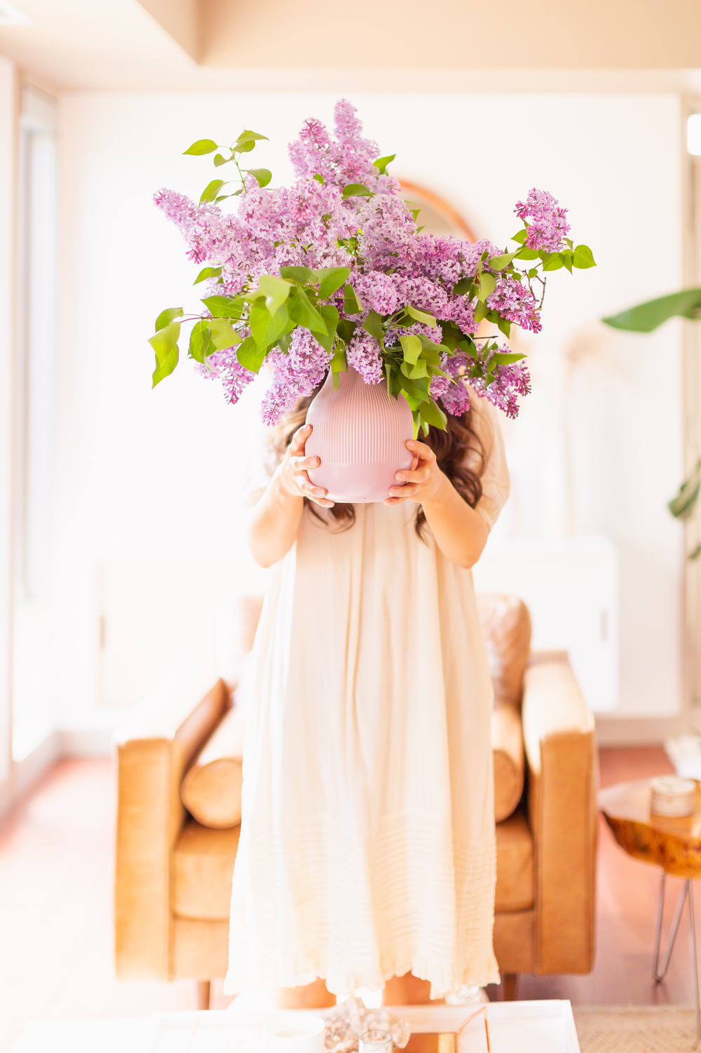How to Create a Lilac Bouquet | Brunette woman in a flowy linen dress holding an oversized lilac arrangement in her neutral mid century meets boho modern living room | DIY Lilac Flower Arrangement | How to Forage Lilacs | How to Prolong Lilac Vase Life | How to Arrange Lilacs | Fresh Lilac Flower Bouquet | Extremely Pretty Lilac Arrangement | Purple Lilac Arrangement | How to Cut Lilacs from a tree or bush | Calgary Creative Lifestyle Blogger // JustineCelina.com