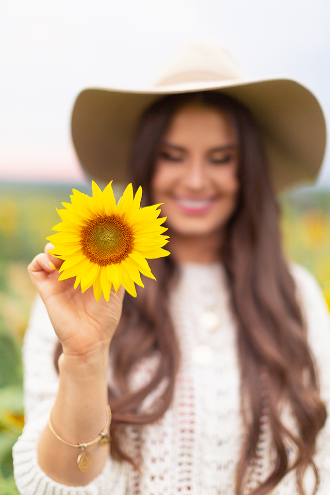 September 2018 Soundtrack | Girl wearing a Hat Holding a Sunflower and Smiling in the Bowden Sunmaze at Sunset, Alberta, Canada | Calgary Lifestyle Blogger // JustineCelina.com