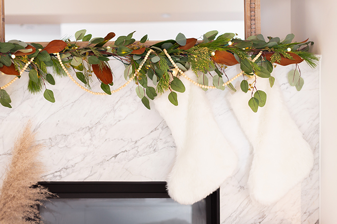 Apartment Friendly Modern Holiday Decor | Canadian Tire CANVAS Pre-lit Eucalyptus Leaves Garland with added greenery, magnolia leaves and wooden beads | Marble Fireplace | Bohemian, Mid Century Modern Holiday Decor | Simple Holiday Arrangement on a Coffee Table with Greenery and Cotton Stems | Bohemian, Mid Century Modern Holiday Decor | Bohemian Holiday Home Tour 2018 | Caramel Mid Century Modern Leather Couches | Canadian Tire CANVAS Ornaments // JustineCelina.com