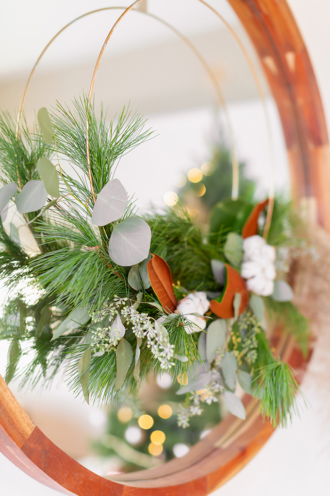 Apartment Friendly Modern Holiday Decor | DIY Modern Holiday Wreath with Magnolia Leaves, Cotton, Silver Dollar Eucalyptus, Seeded Eucalyptus, Cedar and Insense Cedar hung over a round wooden frame mirror | Bohemian, Mid Century Modern Holiday Decor | Bohemian Holiday Home Tour 2018 | Caramel Mid Century Modern Leather Couches | Canadian Tire CANVAS Ornaments // JustineCelina.com 