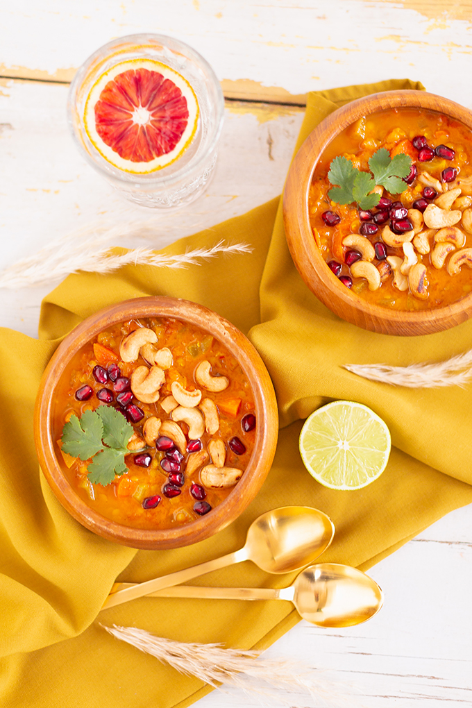 Slow Cooker Vegan Mulligatawny Soup with Red Lentils | #vegan #glutenfree | A warm bowl of vegan mulligatawny soup garnished with roasted cashews, pomegranate arils and cilantro with gold spoons and citrus water | The best vegan mulligatawny soup slow cooker recipe | vegetarian mulligatawny soup | vegetarian mulligatawny soup recipe lentils | vegetarian mulligatawny soup slow cooker | mulligatawny soup crock pot | best winter vegan slow cooker recipes // JustineCelina.com