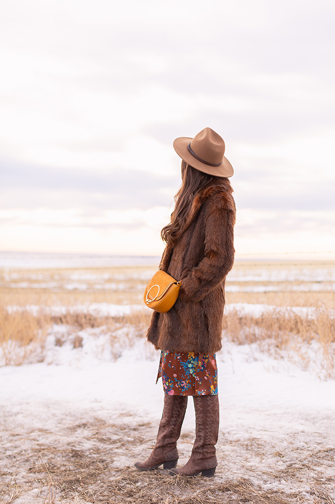  Pre Spring 2019 Trend Guide Bohemian Rhapsody: How to Style Midi Dresses for Transitional Spring Weather | Brunette Girl Standing in a Country Field at Sunrise Wearing a Brown Faux Fur Coat, Brown Floral Dress, Brown Wide Brim Hat and a Mustard Cross Body Bag | Bohemian Winter Style Ideas | Pantone Spring Summer 2019 Fashion Ideas | Calgary, Alberta, Canada Fashion & Lifestyle Blogger // JustineCelina.com