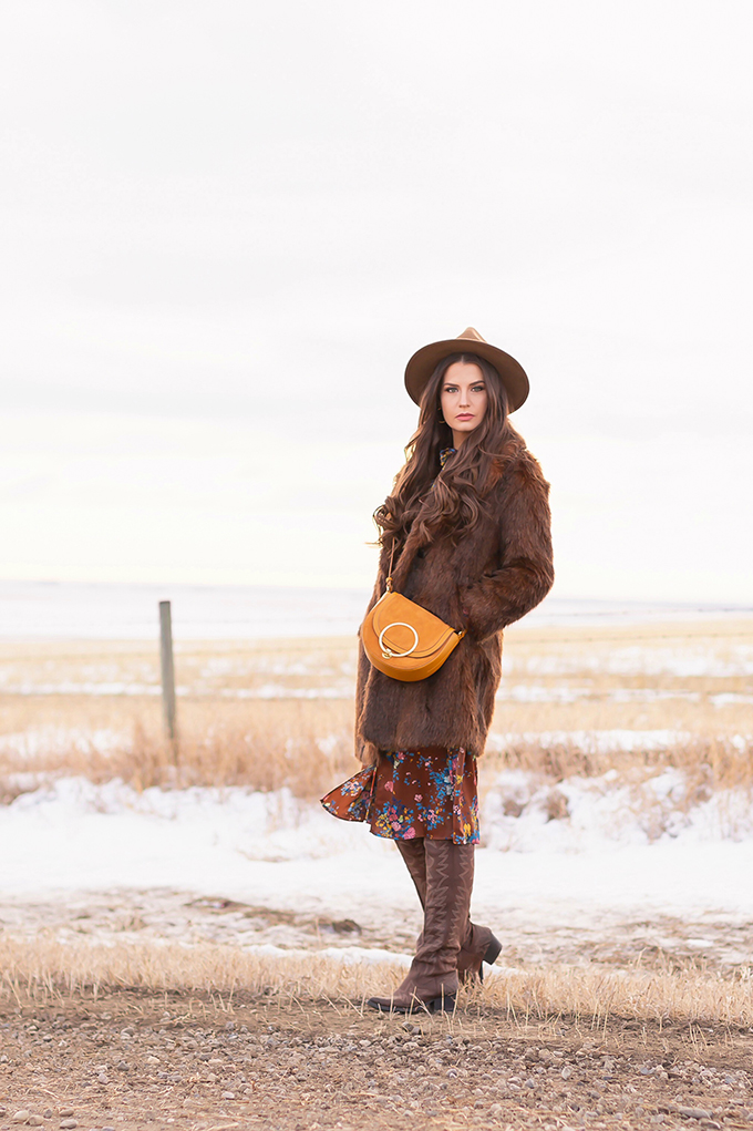  Pre Spring 2019 Trend Guide Bohemian Rhapsody: How to Style Midi Dresses for Transitional Spring Weather | Brunette Girl Standing in a Country Field at Sunrise Wearing a Brown Faux Fur Coat, Brown Floral Dress, Brown Wide Brim Hat and a Mustard Cross Body Bag | Bohemian Winter Style Ideas | Pantone Spring Summer 2019 Fashion Ideas | Calgary, Alberta, Canada Fashion & Lifestyle Blogger // JustineCelina.com