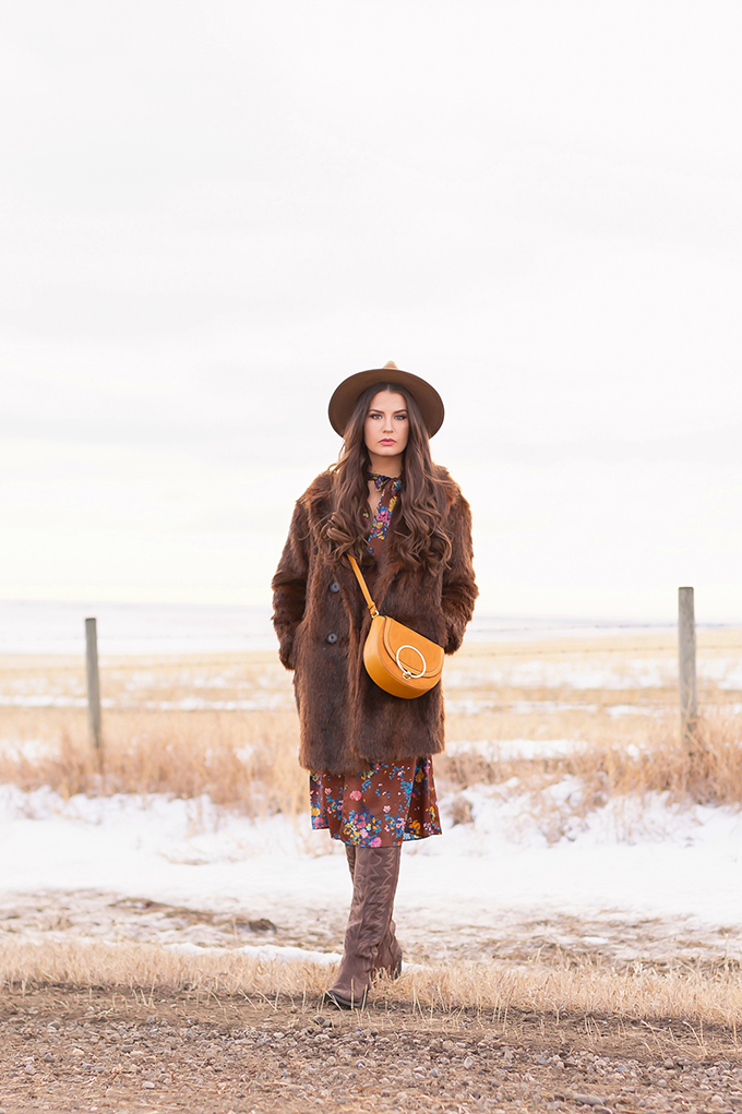  Pre Spring 2019 Trend Guide Bohemian Rhapsody: How to Style Midi Dresses for Transitional Spring Weather | Brunette Girl Standing in a Country Field at Sunrise Wearing a Brown Faux Fur Coat, Brown Floral Dress, Brown Wide Brim Hat and a Mustard Cross Body Bag | Bohemian Winter Style Ideas | Pantone Spring Summer 2019 Fashion Ideas | Calgary, Alberta, Canada Fashion & Lifestyle Blogger // JustineCelina.com