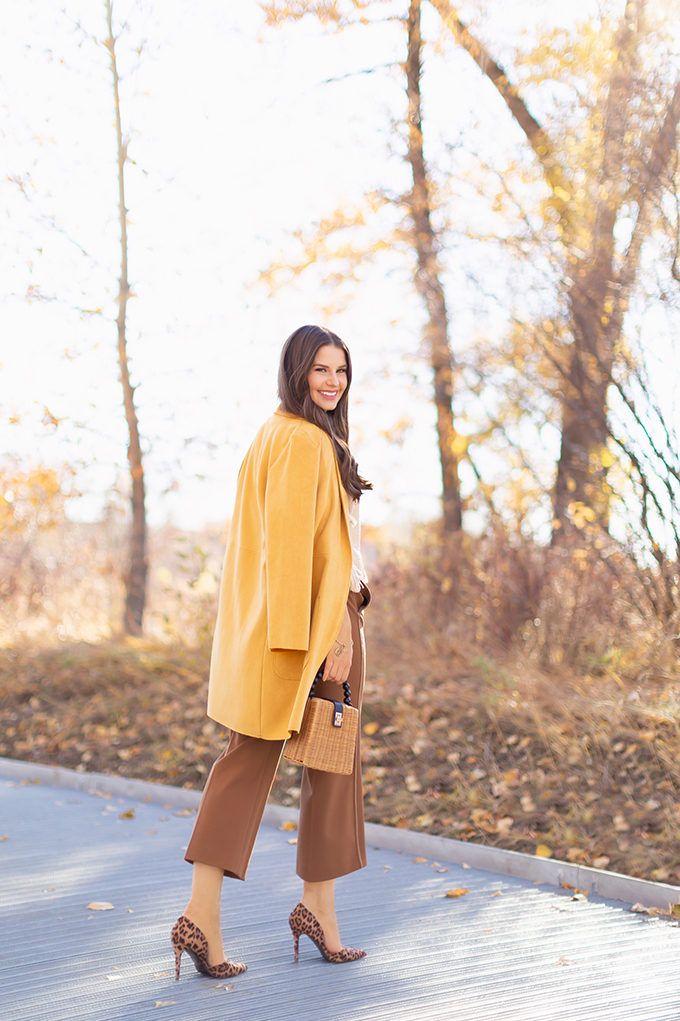 WORK WEAR | SPRING 2019 TRENDS AT THE OFFICE | How to Style Culottes for the Office | Brown 70’s Style Culottes with a Mustard Faux Suede Jacket, Knit Fringe Hem Top, Natural Material Rattan Woven Box Bag and Leopard Print D’Orsay Heels | Spring 2019 Trends | Office Appropriate Spring Outfit Ideas // JustineCelina.com