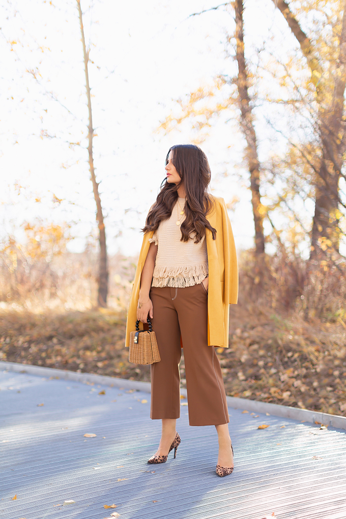 WORK WEAR | SPRING 2019 TRENDS AT THE OFFICE | How to Style Culottes for the Office | Brown 70’s Style Culottes with a Mustard Faux Suede Jacket, Knit Fringe Hem Top, Natural Material Rattan Woven Box Bag and Leopard Print D’Orsay Heels | Spring 2019 Trends | Office Appropriate Spring Outfit Ideas // JustineCelina.com