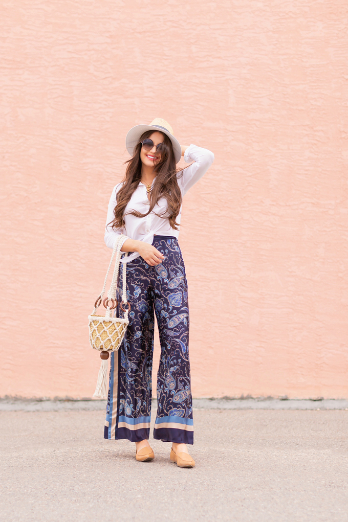 Out of Office | Brunette woman wearing paisley palazzo pants, a white linen shirt, a straw fedora, a macrame bucket bag, leather pointed toe flats and round sunglasses | Canadian May Long Weekend Outfit Ideas | Roadtrip Outfit Ideas | Calgary Fashion & Lifestyle Blogger // JustineCelina.com