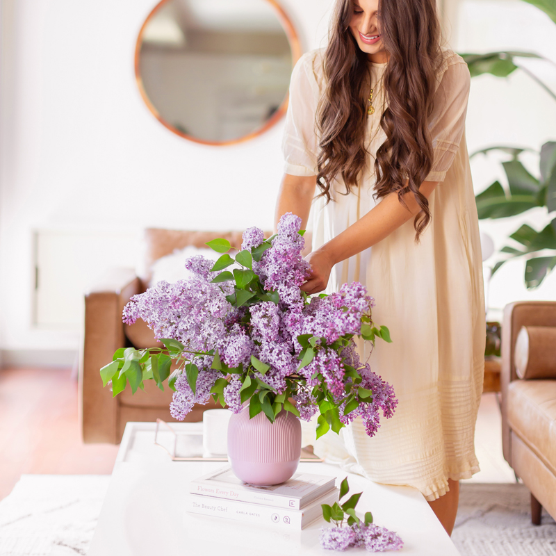 June 2019 Soundtrack | Smiling brunette woman in a flowy linen dress creating an oversized lilac arrangement in her mid century modern living room // JustineCelina.com