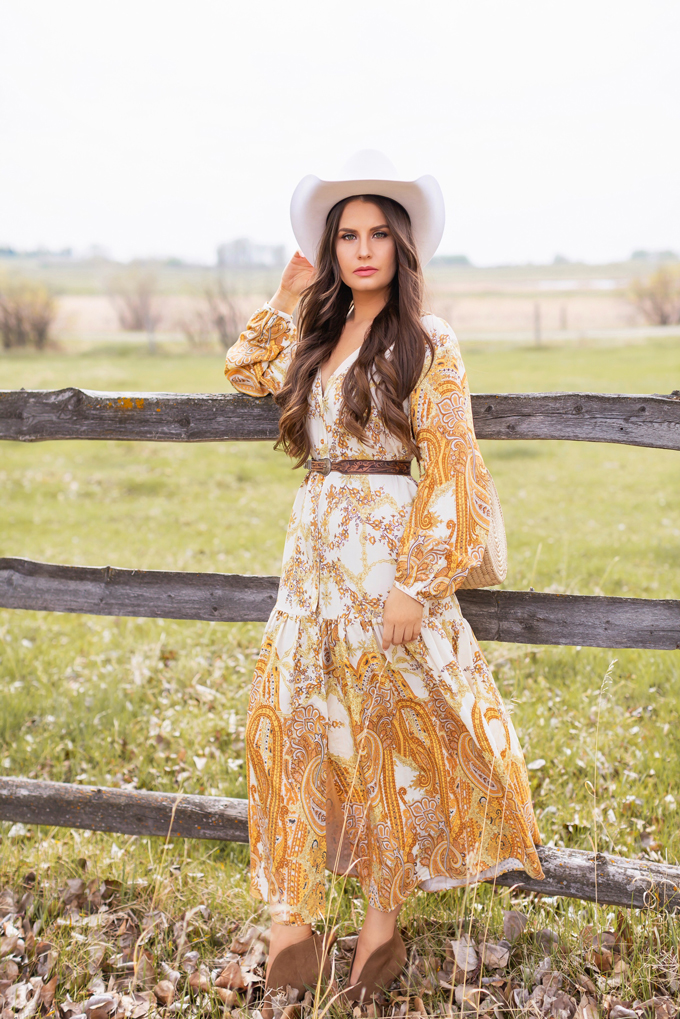 How to Style | Calgary’s White Hat for The Stampede | Stampede 2019 Outfit Ideas | Brunette Woman wearing a flow Paisley dress with a vintage western belt, Smithbilt The White Hat in White Felt and mid heel ankle boots with a round rattan bag | Smithbilt White Hat Outfit | How to Style a Cowboy Hat for the Calgary Stampede | Calgary Stampede Dress Code | Bohemian Western Inspired Outfit Summer 2019 | Boho Stampede Style | Justine Celina Maguire x Tourism Calgary // JustineCelina.com