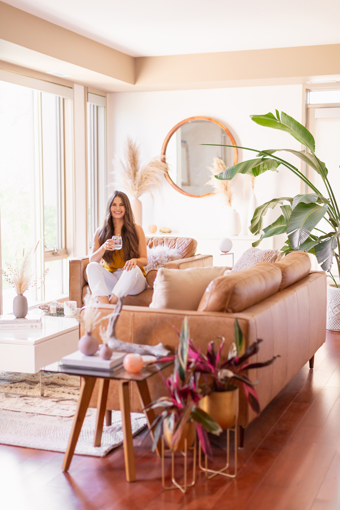 MidSummer Space Refresh Update | Smiling brunette woman enjoying a glass of white wine in her bright and airy mid century modern living room during the summer | Brunette woman wearing a knit tank top and white cropped jeans sitting on her coffee table | A Bohemian, Mid-Century Modern Living Room featuring Pampas Grass | Summer Decor 2019 Trends | Bohemian, Mid Century Modern Decor | Calgary Lifestyle, Interior Design and Home Decor Blogger // JustineCelina.com