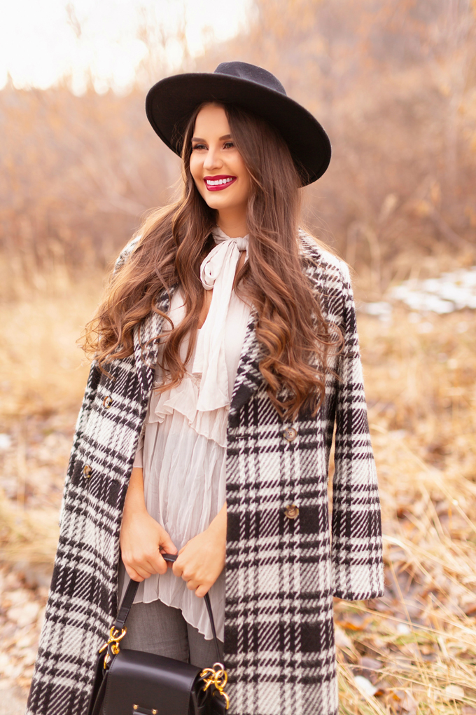 Autumn / Winter 2019 Lookbook: Checked Cowgirl | Top Fall / Winter 2019 / 2020 Trends | Top Winter 2019 Trends and How to Wear Them | Smiling Brunette woman wearing a Vero Moda Wool Plaid Coat, Ruffled, Tie Neck Blouse, Bite Beauty’s Amuse Bouche Lipstick in Beetroot and a black wide brimmed black hat | Bohemian Canadian Winter Outfit Ideas | Western Winter Outfit Ideas | How to Style a Plaid Coat | Top Calgary Fashion Blogger // JustineCelina.com