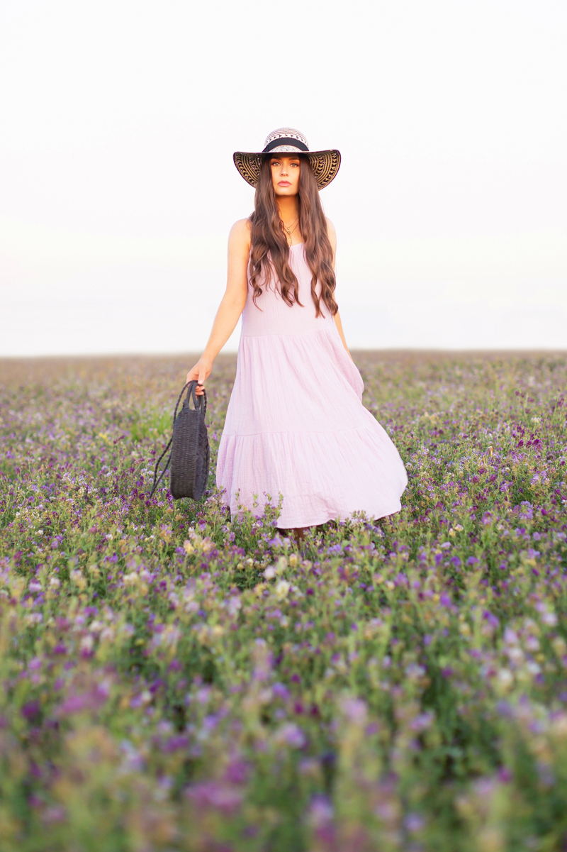 Summer 2020 Lookbook | Boho Summer 2020 Outfit Ideas | Summer Capsule Wardrobe | Summer Quarantine Outfits | Classic Summer Outfit Ideas | The Best Cotton Dresses 2020 | Sunset Photoshoot | Summer to Fall Outfit Ideas | Classic Affordable Summer Style | Summer 2020 Trends | Brunette woman wearing a lilac H&M Crinkled Cotton Dress, Oversized Black Patterned Straw Hat and Black Circular Straw Bag in a field of purple alfalfa at sunset | Calgary Alberta Fashion Blogger // JustineCelina.com