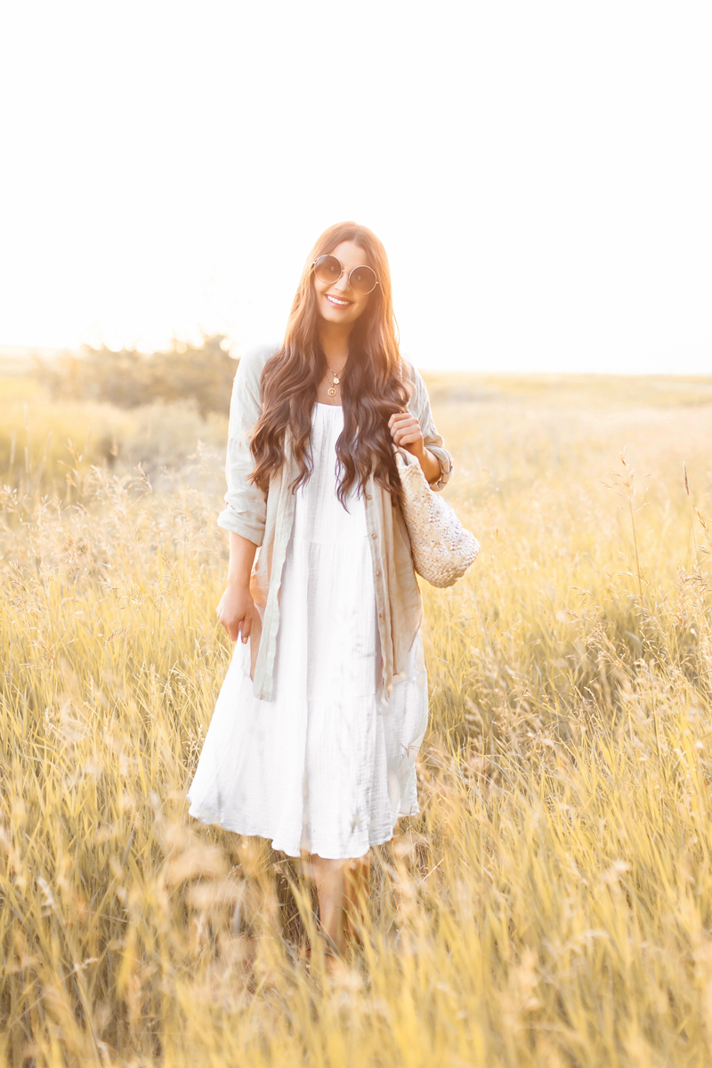 Summer 2020 Lookbook | Boho Summer 2020 Outfit Ideas | Summer Capsule Wardrobe | Summer Quarantine Outfits | Classic Summer Outfit Ideas | The Best Cotton Dresses 2020 | Sunset Photoshoot | Summer to Fall Outfit Ideas | Classic Affordable Summer Style | Summer 2020 Trends | Smiling brunette woman wearing a white H&M Crinkled Cotton Dress, Linen Button Down Shirt, Circular Sunglasses and a Straw tote Bag in a wheat field at sunset | Calgary Alberta Fashion Blogger // JustineCelina.com