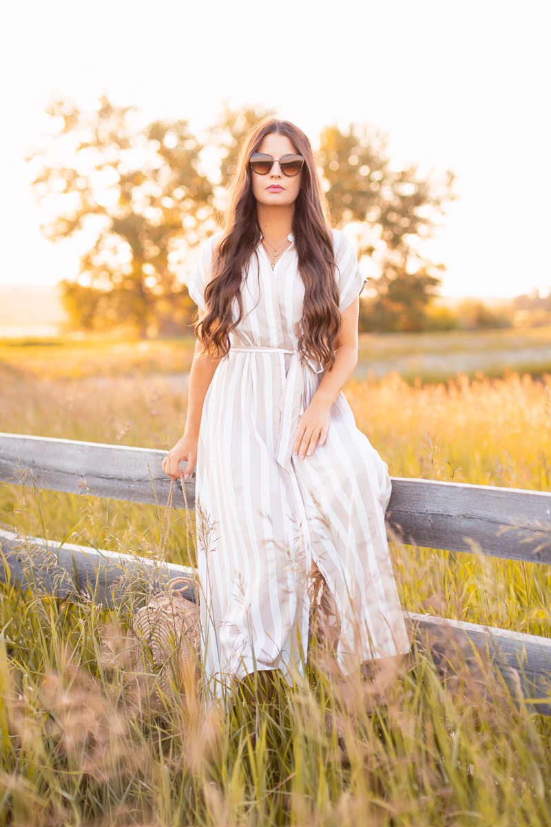 Summer 2020 Lookbook | Boho Summer 2020 Outfit Ideas | Summer Capsule Wardrobe | Summer Quarantine Outfits | Classic Summer Outfit Ideas | The Best Viscose Dresses 2020 | Summer to Fall Outfit Ideas | Classic Affordable Summer Style | Summer 2020 Trends | Elegant midi dresses | Brunette woman sitting on a fence wearing a Beige/white striped H&M Button-front Dress, cat eye sunglasses artisan woven circular bag in Wheatland County at sunset | Calgary Alberta Fashion Blogger // JustineCelina.com