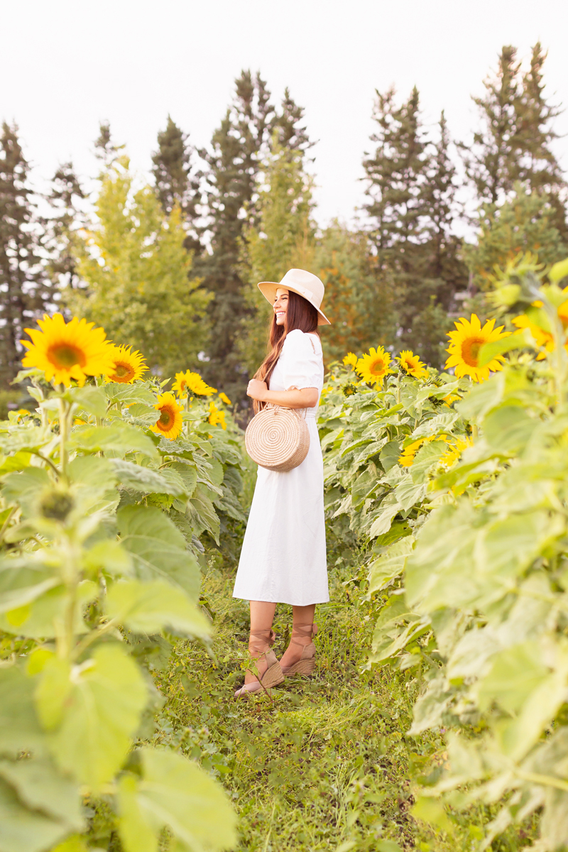 A Guide to Bowden SunMaze & Eagle Creek Farms | Bowden SunMaze September 2020 | Sunflower Field Near Me | The Best Alberta Sunflower Field | Alberta Sunflower U-Pick | Bowden SunMaze Sunflower Field Best Time To Go | Bowden SunMaze Cost | Eagle Creek Farms Review | Sunflower Field Instagram Tips | Cottagecore Aesthetic | Smiling brunette woman wearing a cream Crêped Cotton Dress and woven fedora laughing in a field of sunflowers at sunset | Calgary Lifestyle Blogger // JustineCelina.com