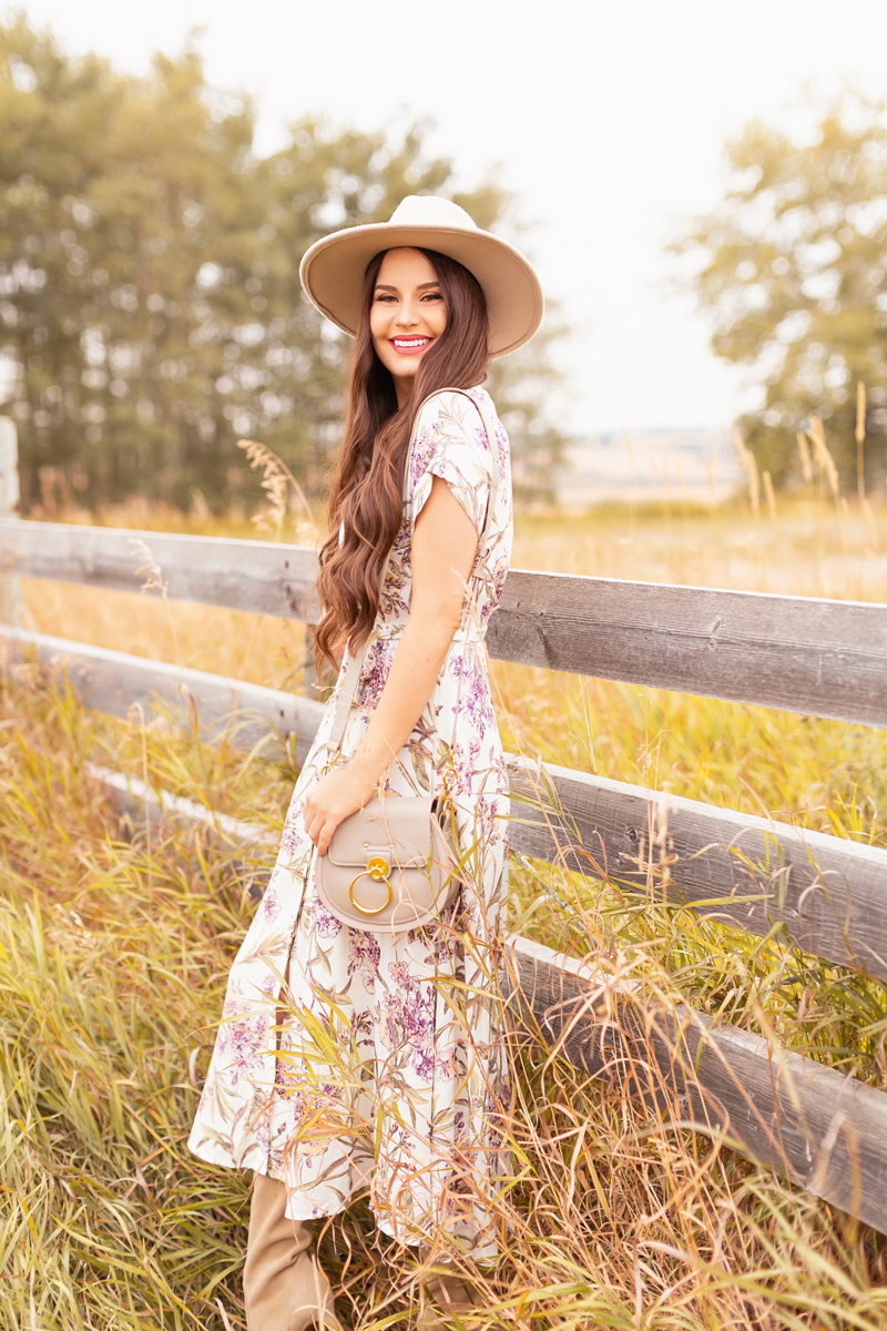 Early Autumn 2020 Lookbook | Country Checks | Brunette woman wearing a botanical print button down midi dress, a Chloe Tess Bag in Grey, knee high suede pointed toe boots and a taupe flat brimmed hat next to an weathered fence in the prairies | Boho Fall 2020 Outfit Ideas | Top Fall 2020 Trends | How to Style Midi Dresses for Fall | Bohemian Fall outfit Ideas | How to Wear Florals in Fall | Cottagecore Fall Outfit Ideas | Calgary Alberta Fashion & Lifestyle Blogger // JustineCelina.com