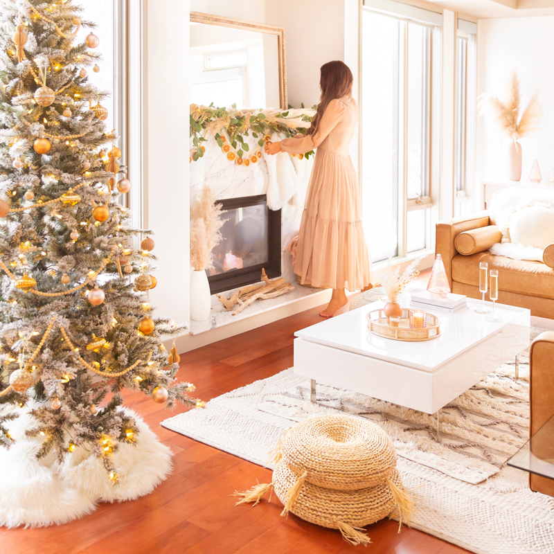 Mid Century Meets Boho Holiday Decor | Brunette woman wearing a taupe chiffon maxi dress hanging stockings in a bright and airy bohemian living room decorating for Christmas | Flocked Christmas Tree with Wood Garland, Metallic and Wood Ornaments | Bohemian Holiday Home Tour 2020 | Boho Chic Christmas Decor | DIY boho dried orange garland | Glam neutral holiday decor | Pampas Grass holiday decor | Pampas Grass Garland | Boho Christmas Tree | Canadian Tire CANVAS Ornaments // JustineCelina.com