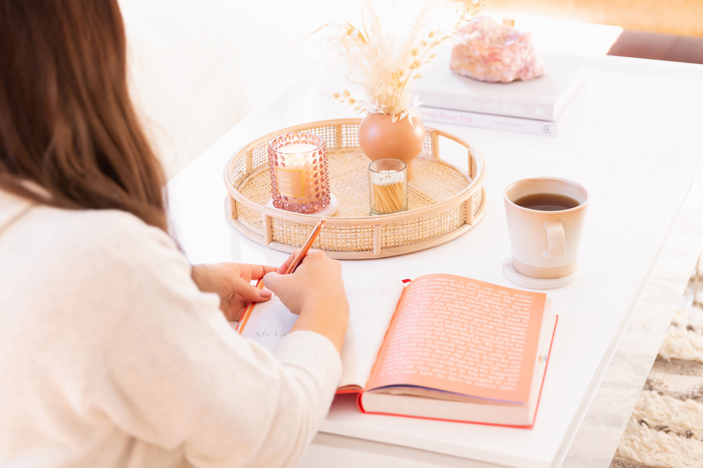 Woman journalling on a coffee table with a candle and cup of coffee in a bright and airy living room | Calgary Lifestyle Blogger // JustineCelina.com