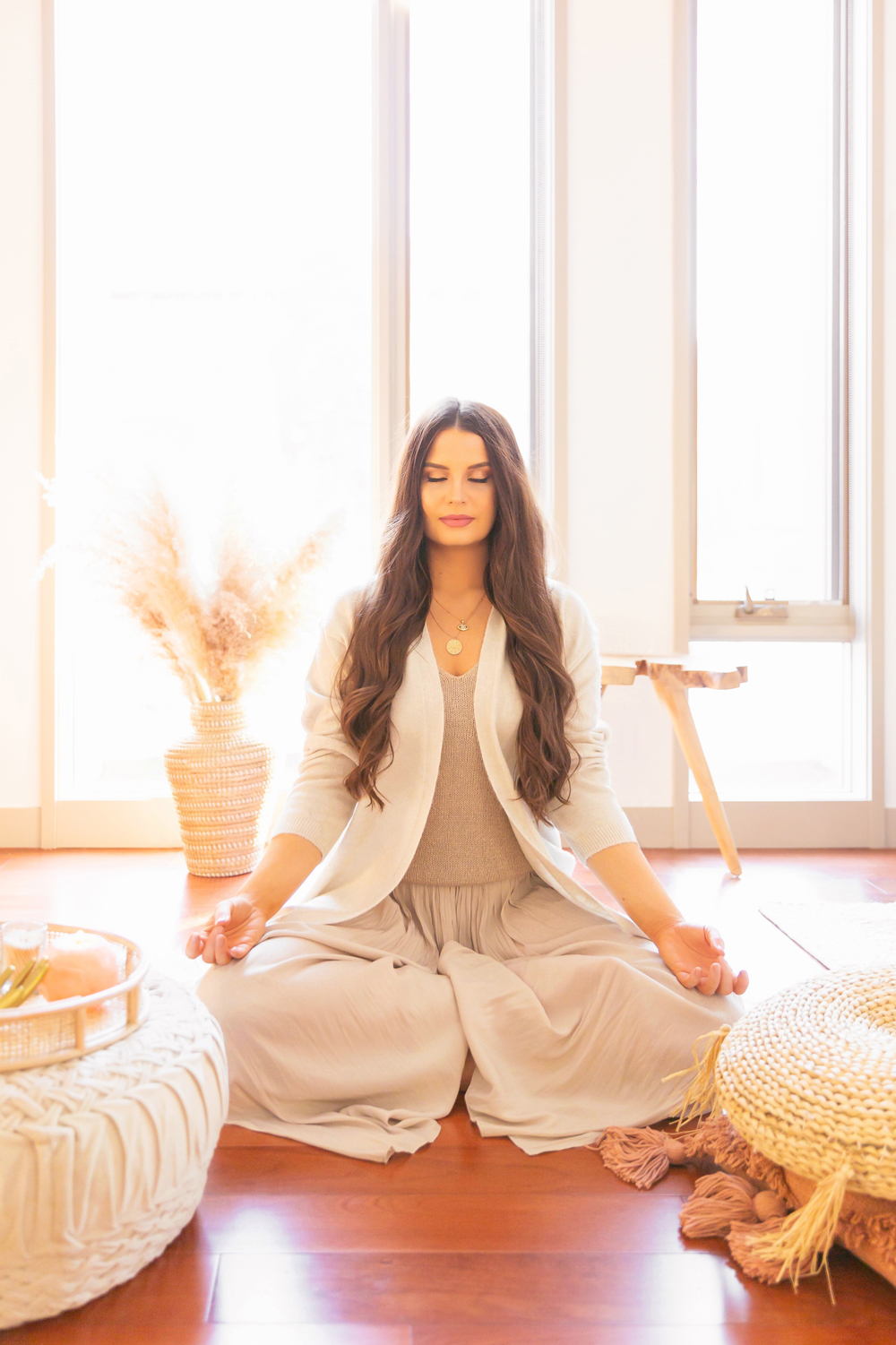 Brunette woman in a casual cream loungewear meditating in bright and airy boho living room | Calgary Lifestyle Blogger // JustineCelina.com