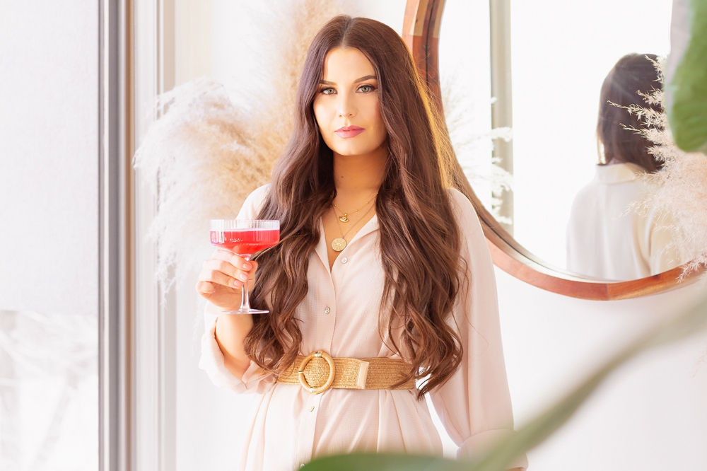 Brunette woman holding a champagne coupe of watermelon kombucha in a bright and airy living room | Calgary Lifestyle Blogger // JustineCelina.com