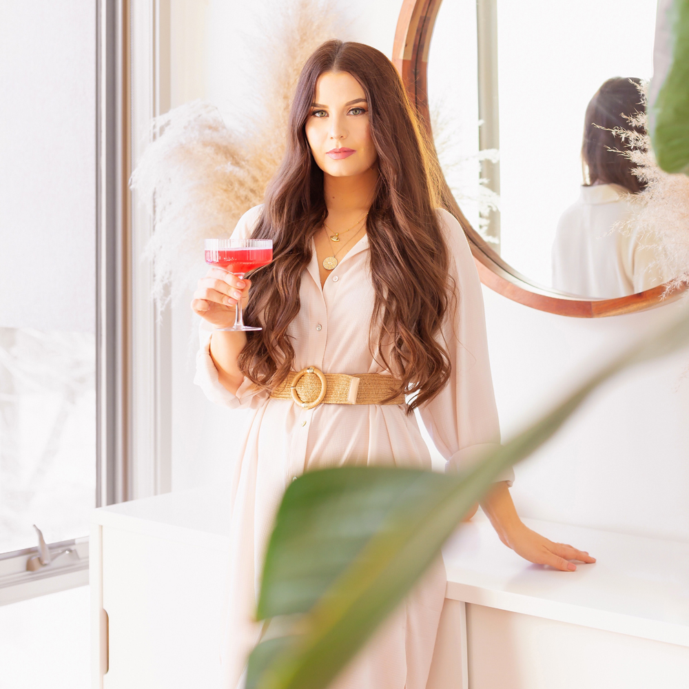 My Dry January Experience | Smiling brunette woman holding a champagne flute full of watermelon kombucha in a bright and airy living room | Calgary Lifestyle Blogger // JustineCelina.com