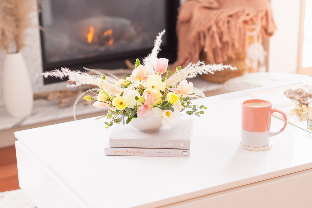 A cheerful spring flower arrangement with pampas grass on white coffee table with a pink mug in front of a white marble fireplace | Calgary Lifestyle Blogger // JustineCelina.com