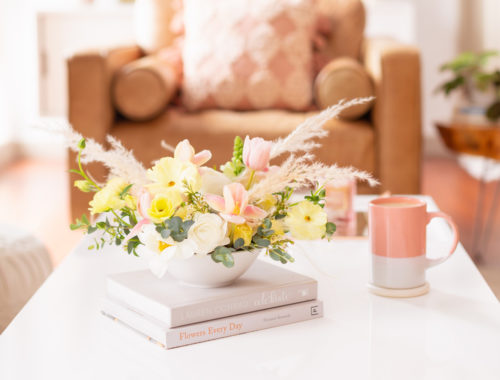 A Pastel Easter Flower Arrangement featuring Quicksand and Spray Roses, Ranunculus and Butterfly Ranunculus, Tulips, Hyacinths, Lisianthus, Eucalyptus, Wax Flowers and Pampas Grass on white coffee table with a pink mug in bright and airy boho living room | Calgary Lifestyle Blogger // JustineCelina.com