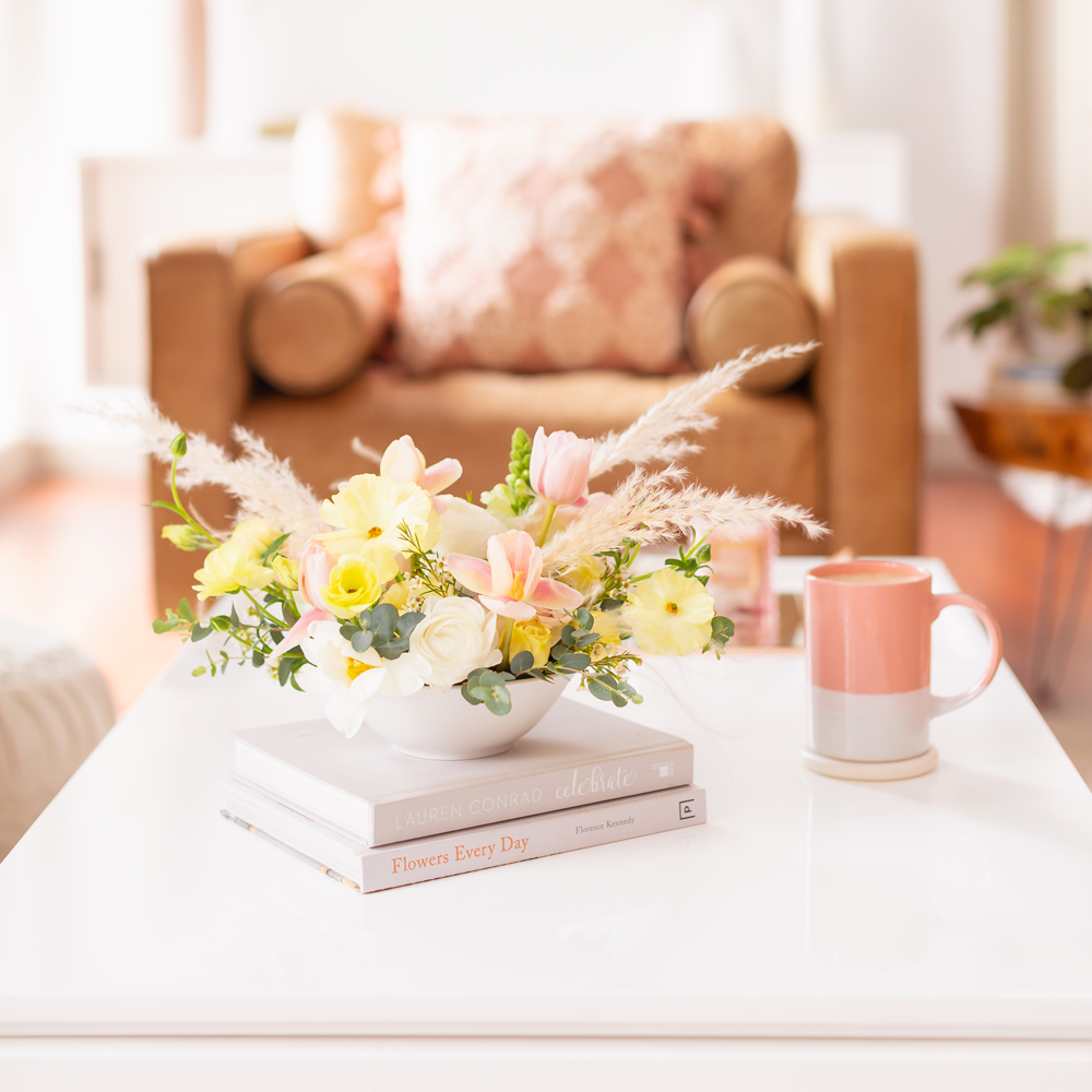 A Pastel Easter Flower Arrangement featuring Quicksand and Spray Roses, Ranunculus and Butterfly Ranunculus, Tulips, Hyacinths, Lisianthus, Eucalyptus, Wax Flowers and Pampas Grass on white coffee table with a pink mug in bright and airy boho living room | Calgary Lifestyle Blogger // JustineCelina.com
