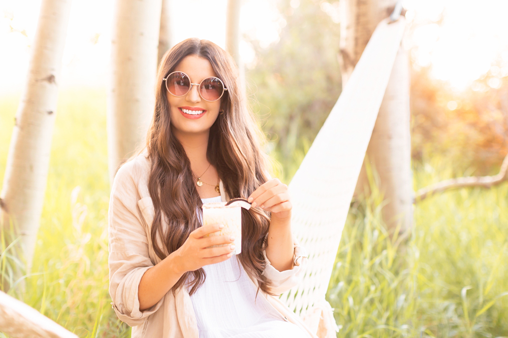 5 Festive Cinco de Mayo Cocktails | 5 of JustineCelina’s most popular dairy, gluten and refined sugar free vegan tequila & mezcal based cocktail to celebrate Cinco de Mayo | Smiling brunette woman wearing a linen shirt and sunglasses holding a margarita in a hammock on a sunny day | Calgary Cocktail Blogger // JustineCelina.com