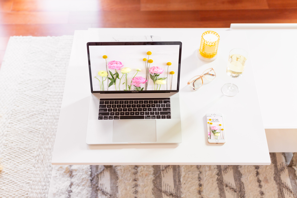 DIGITAL BLOOMS JULY 2021 | 11 Free Downloadable Floral Tech Backgrounds for Summer | Feminine WFH set up with a MacBook Pro and iPhone featuring JustineCelina’sJuly Digital Blooms floral tech wallpaper, a glass of white wine and a yellow candle in a bright and sunny bohemian Living Room | Female Entrepreneur Digital Wallpapers | The Best of Justine Celina’s Summer Digital Blooms | Summer Flower Desktop Wallpaper | Calgary Creative Lifestyle Blogger // JustineCelina.com