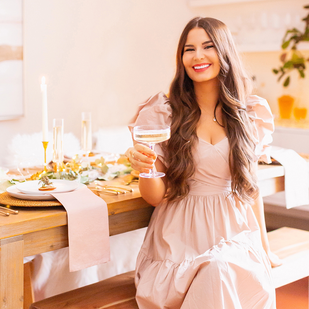 Meet Justine // Justine Celina Maguire | Calgary Lifestyle Blogger | Entertaining in Justine Celina Maguire’s boho meets mid century modern apartment | Smiling brunette woman wearing a blush pink dress sitting at a beautiful neutral tablescape with a holding a champagne coupe | Calgary, Alberta, Canada Creative Lifestyle Blogger and Entrepreneur // JustineCelina.com