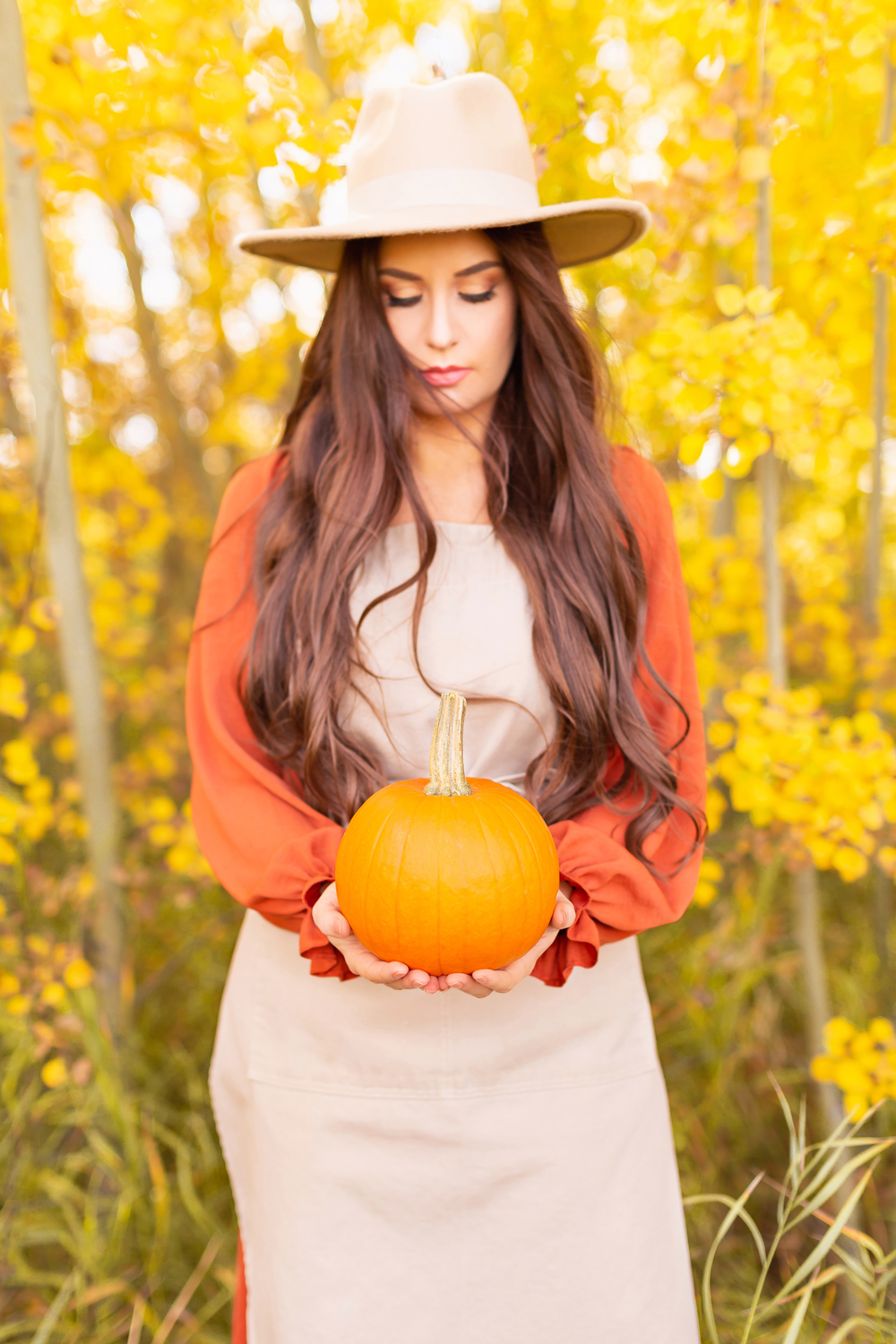 Plant Based Pumpkin Recipes to Try This Fall {Dairy Free, Gluten Free, Refined Sugar Free} | Brunette woman wearing a hat and gardening apron holding a home grown garden sugar pumpkin against a backdrop of yellow leaves | Easy Vegan Pumpkin Recipes | Healthy Vegan Pumpkin Recipes | Vegan Pumpkin Snacks | The best plant based pumpkin recipes | Garden pumpkin recipes | Zone 3b Garden | JustineCelina’s Country Garden 2021 | Calgary Canada Plant Based Food and Garden Blogger // JustineCelina.com