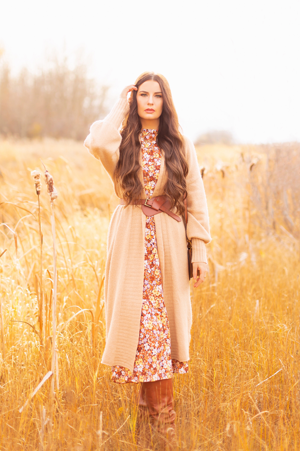 6 Luxe Bohemian Fall Outfits | Elegant Equestrian | Brunette woman  wearing a fall floral midi dress, a longline camel cardigan, a cognac leather corset belt and a round cognac crossbody bag amongst golden grasses and cattails | Boho Fall 2022 Outfit Ideas | Classic Fall Outfit Formulas | Feminine Bohemian Style | Polished Bohemian Style | Elegant Bohemian Style | Bohemian Outfit Ideas | Boho Fall Accessories | Calgary Alberta Fashion Blogger // JustineCelina.com