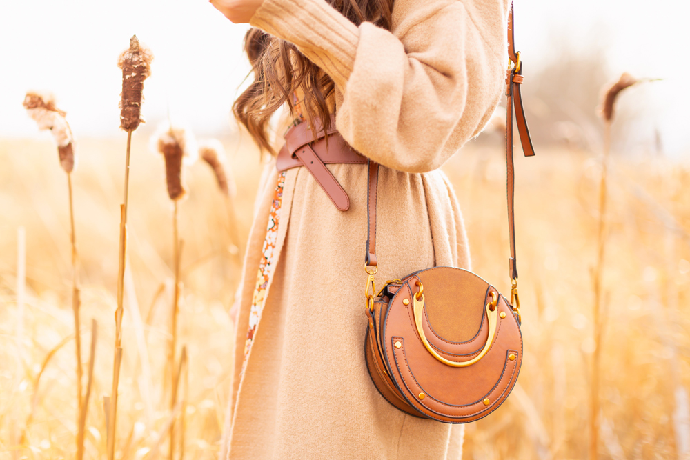 6 Luxe Bohemian Fall Outfits | Elegant Equestrian | Detail photo of a woman wearing a fall floral midi dress, a longline camel cardigan, a cognac leather corset belt and a round cognac crossbody bag amongst golden grasses and cattails | Boho Fall 2022 Outfit Ideas | Classic Fall Outfit Formulas | Feminine Bohemian Style | Polished Bohemian Style | Elegant Bohemian Style | Bohemian Outfit Ideas | Boho Fall Accessories | Calgary Alberta Fashion Blogger // JustineCelina.com