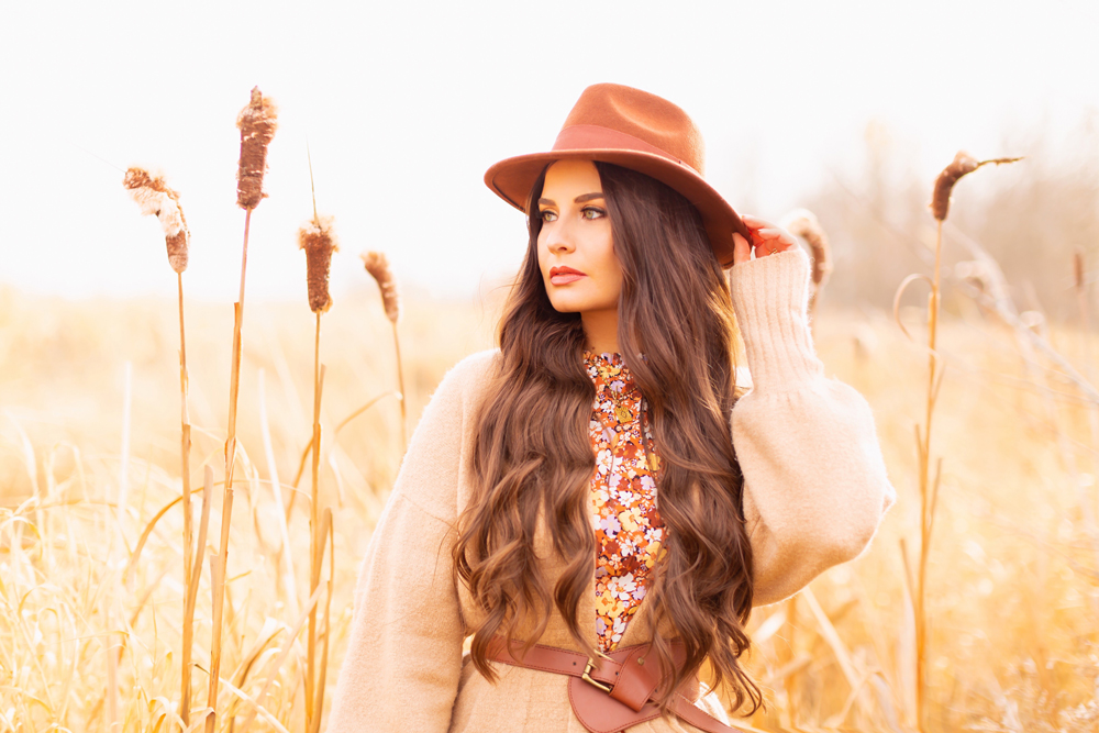 6 Luxe Bohemian Fall Outfits | Elegant Equestrian | Brunette woman  wearing a fall floral midi dress, a longline camel cardigan, a cognac leather corset belt and a round cognac crossbody bag amongst golden grasses and cattails | Boho Fall 2022 Outfit Ideas | Classic Fall Outfit Formulas | Feminine Bohemian Style | Polished Bohemian Style | Elegant Bohemian Style | Bohemian Outfit Ideas | Boho Fall Accessories | Calgary Alberta Fashion Blogger // JustineCelina.com