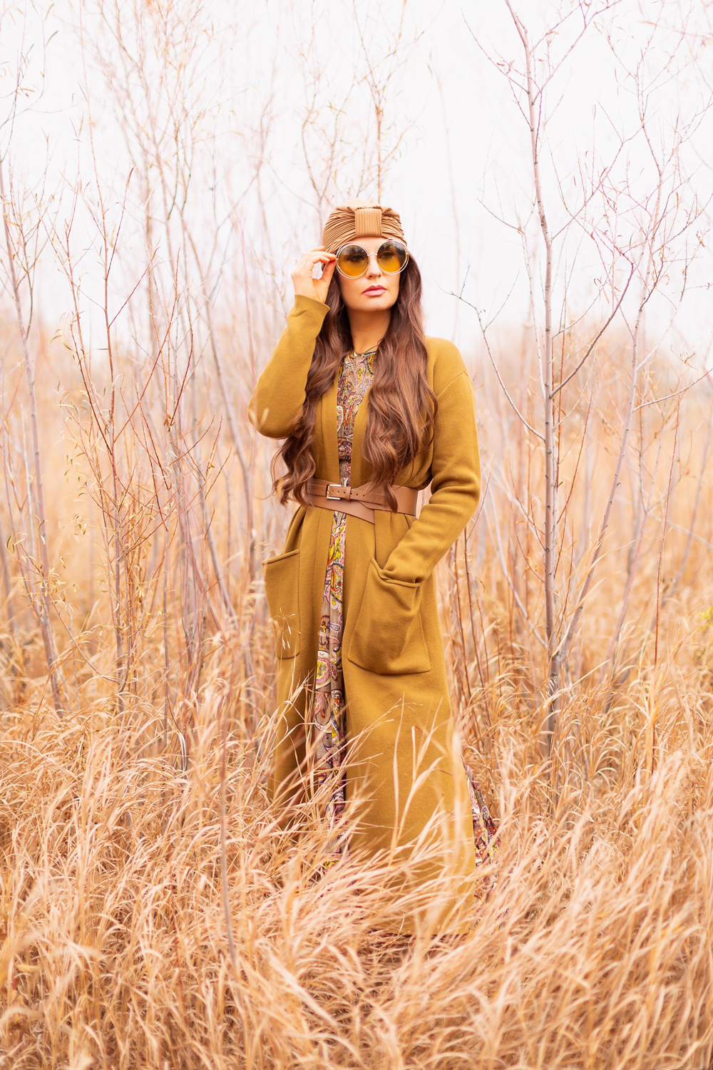 6 Luxe Bohemian Fall Outfits | Organic Olive | Brunette woman wearing an olive paisley maxi dress, longline olive green cardigan, taupe corset belt, exotic taupe hat an oversized round olive sunglasses amongst wild fall grasses in a willow grove | Boho Fall 2022 Outfit Ideas | Feminine Bohemian Style | Polished Bohemian Style | Elegant Bohemian Style | Bohemian Outfit Ideas | How to Style a Paisley Maxi Dress for Fall | Calgary Alberta Fashion Blogger // JustineCelina.com