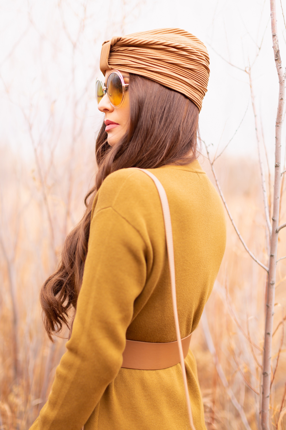 6 Luxe Bohemian Fall Outfits | Organic Olive | Brunette woman wearing a longline olive green cardigan, taupe corset belt, exotic taupe hat an oversized round olive sunglasses amongst wild fall grasses in a willow grove | Boho Fall 2022 Outfit Ideas | Feminine Bohemian Style | Polished Bohemian Style | Elegant Bohemian Style | Bohemian Outfit Ideas | How to Style a Paisley Maxi Dress for Fall | Calgary Alberta Fashion Blogger // JustineCelina.com