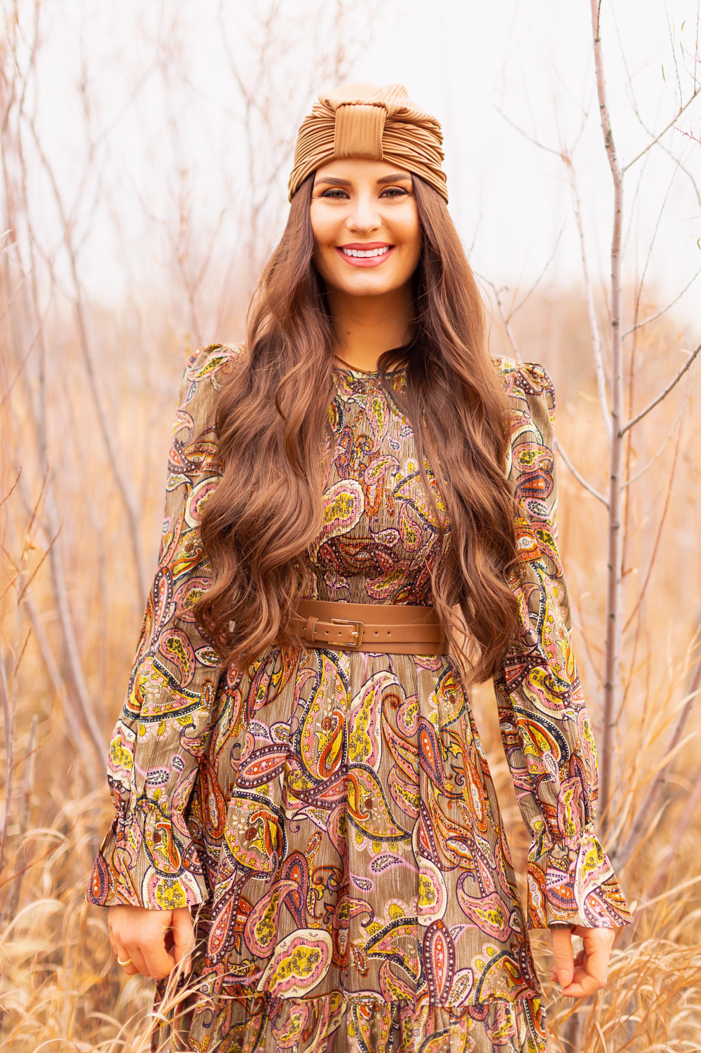 6 Luxe Bohemian Fall Outfits | Organic Olive | Smiling brunette woman with wavy waist long hair wearing an olive paisley maxi dress, taupe corset belt and an exotic taupe hat  amongst wild fall grasses in a willow grove | Boho Fall 2022 Outfit Ideas | Feminine Bohemian Style | Polished Bohemian Style | Elegant Bohemian Style | Bohemian Outfit Ideas | How to Style a Paisley Maxi Dress for Fall | Calgary Alberta Fashion Blogger // JustineCelina.com