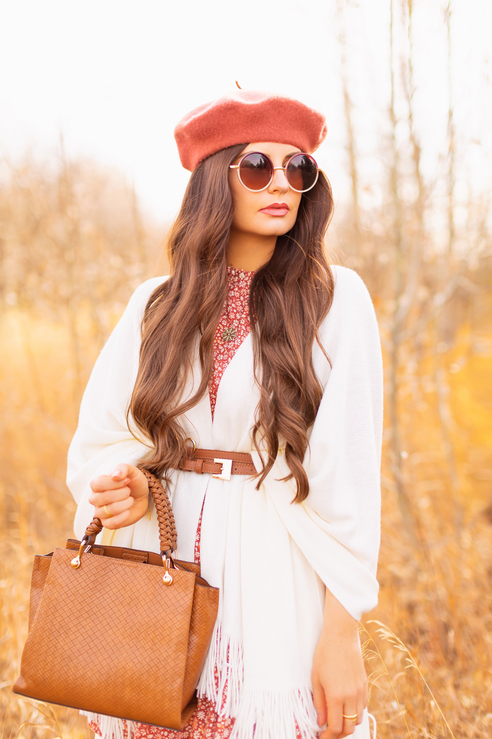 6 Luxe Bohemian Fall Outfits | Playful Poncho | Brunette woman wearing a fall floral mini dress, a cream fringe trimmed poncho, a cognac leather corset belt, a rust fedora, a woven cognac crossbody bag and round gradient sunglasses amongst golden grasses and trees | Boho Fall 2022 Outfit Ideas | Classic Fall Outfit Formulas | Feminine Bohemian Style | Polished Bohemian Style | Elegant Bohemian Style | Bohemian Outfit Ideas | Calgary Alberta Fashion Blogger // JustineCelina.com
