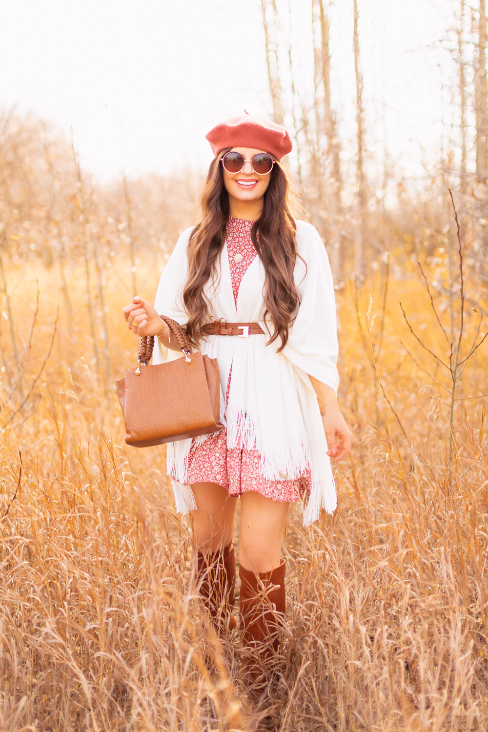 6 Luxe Bohemian Fall Outfits | Playful Poncho | Brunette woman wearing a fall floral mini dress, a cream fringe trimmed poncho, a cognac leather corset belt, cognac western knee high boots, a rust fedora and a woven cognac crossbody bag amongst golden grasses and trees | Boho Fall 2022 Outfit Ideas | Classic Fall Outfit Formulas | Feminine Bohemian Style | Polished Bohemian Style | Elegant Bohemian Style | Bohemian Outfit Ideas | Calgary Alberta Fashion Blogger // JustineCelina.com
