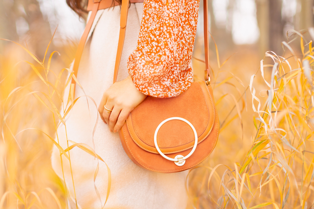 6 Luxe Bohemian Fall Outfits | Rancher Revival | Woman wearing an orange floral mini dress with long sleeves, beige Pink Martini Stockport Vest, wide cognac waist belt with tie detail and a crossbody cognac suede saddle bag amoungst golden grasses and bare trees | Boho Fall 2022 Outfit Ideas | Classic Fall Outfit Formulas | Feminine Bohemian Style | Bohemian Outfit Ideas | How to Style a Rancher Hat | Calgary Alberta Fashion Blogger // JustineCelina.com