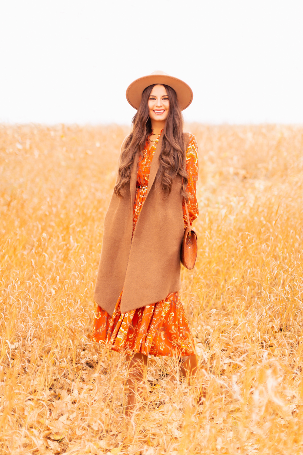 6 Luxe Bohemian Fall Outfits | Thanksgiving Chic | Smiling brunette woman wearing an orange paisley midi dress, brown Pink Martini Stockport Vest, a slim cognac leather corset, a vintage leather hand tooled bag and a camel flat brimmed rancher hat amongst golden grasses | Boho Fall 2022 Outfit Ideas | Classic Fall Outfit Formulas | Feminine Bohemian Style | Polished Bohemian Style | Elegant Bohemian Style | Bohemian Outfit Ideas | Calgary Alberta Fashion Blogger // JustineCelina.com
