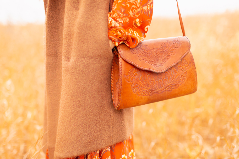 6 Luxe Bohemian Fall Outfits | Thanksgiving Chic | Detail photo of a woman wearing an orange paisley midi dress, brown Pink Martini Stockport Vest and a vintage leather hand tooled bag amoungst golden grasses | Boho Fall 2022 Outfit Ideas | Classic Fall Outfit Formulas | Feminine Bohemian Style | Polished Bohemian Style | Elegant Bohemian Style | Bohemian Outfit Ideas | Calgary Alberta Fashion Blogger // JustineCelina.com